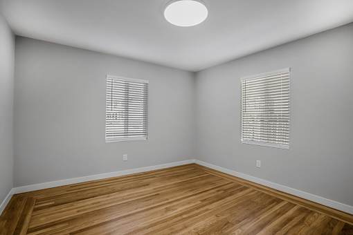 A room with wooden floors and two windows with blinds.