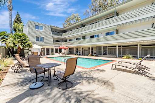 A pool area with chairs and a table in front of a building.
