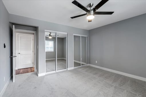 an empty bedroom with a ceiling fan and a mirrored closet