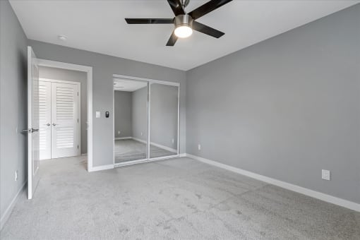 an empty living room with a ceiling fan and a mirrored closet