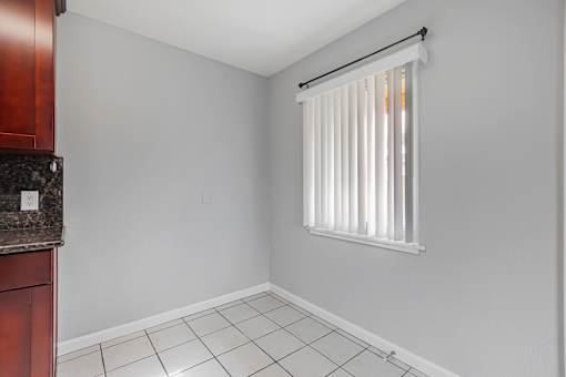 A kitchen with a white tile floor and a window with blinds.