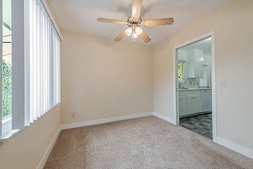A room with a ceiling fan and a doorway leading to a kitchen.