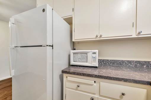 A white refrigerator stands next to a counter with a microwave on it.