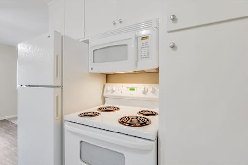 A white kitchen with a stove, microwave, and refrigerator.
