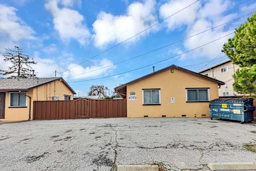 A yellow house with a brown fence and a blue dumpster in front.