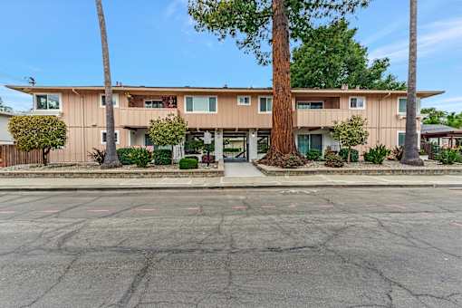 A large tree stands in front of a two-story apartment building.