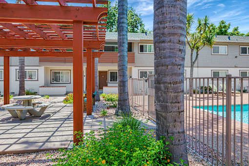 A red pergola is in front of a building with a pool.