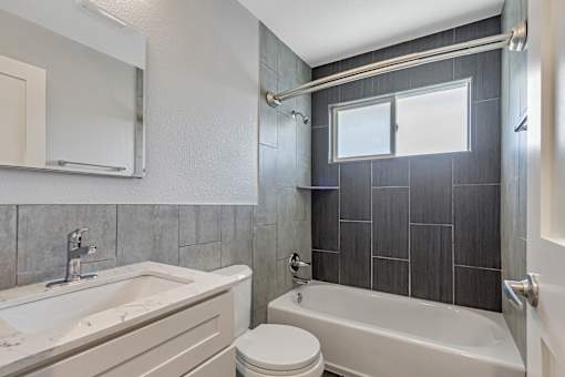 A bathroom with a white tub and toilet, a sink, and a window.