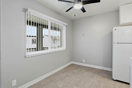 A room with a fan, a window with blinds, and a white refrigerator.