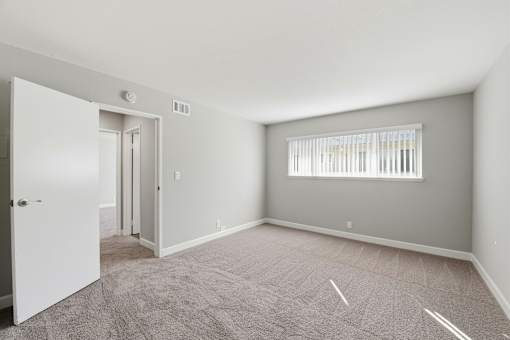 A room with a carpeted floor and a window with blinds.