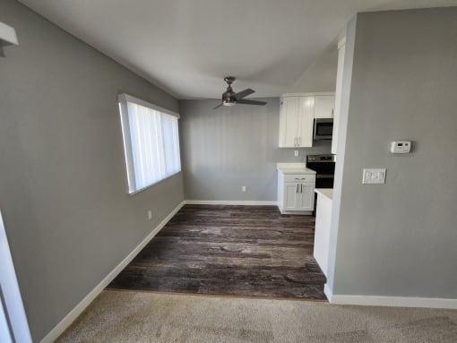 an empty living room with a ceiling fan and a kitchen
