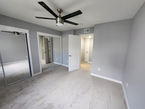 an empty bedroom with a ceiling fan and mirrors