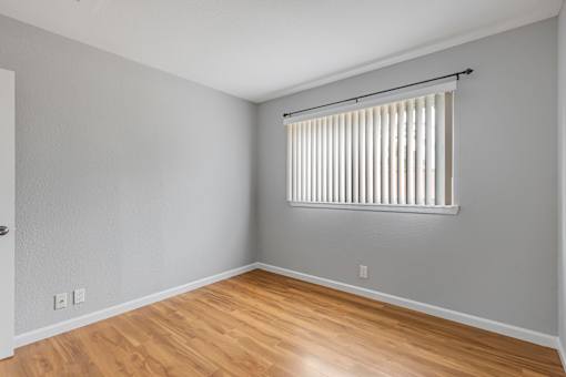 A room with wooden floors and a window with blinds.