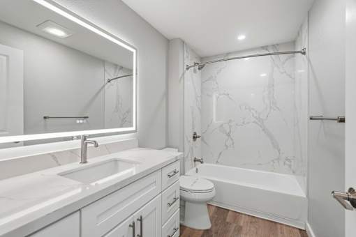 A white bathroom with a marble shower and a white toilet.