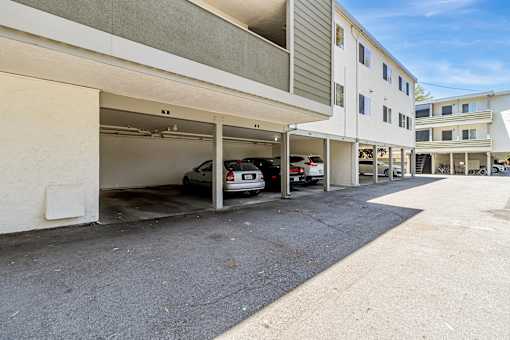 A car is parked in a garage attached to a white building.