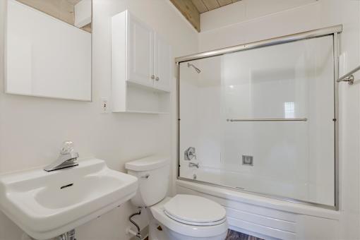 A white bathroom with a sink, toilet, and shower.