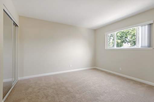 A room with a carpeted floor and a window with white curtains.