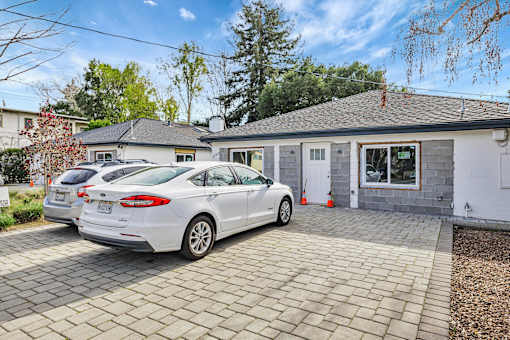 A white car is parked in front of a house with a grey roof.