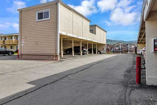 A parking lot with a tan building on the left and a red pole on the right.