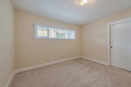 A room with a carpeted floor and a window with blinds.
