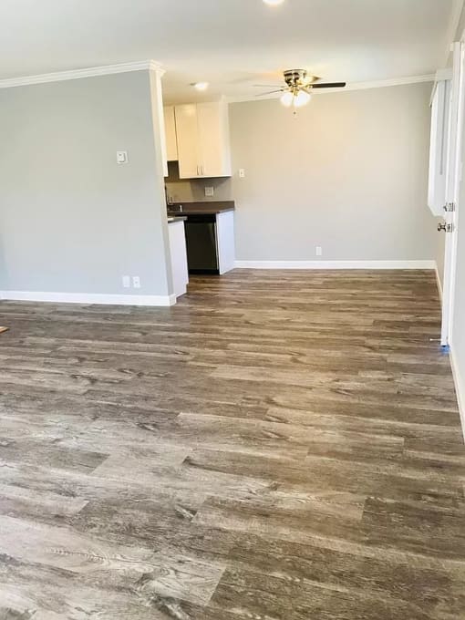 an empty living room with wood flooring and a kitchen