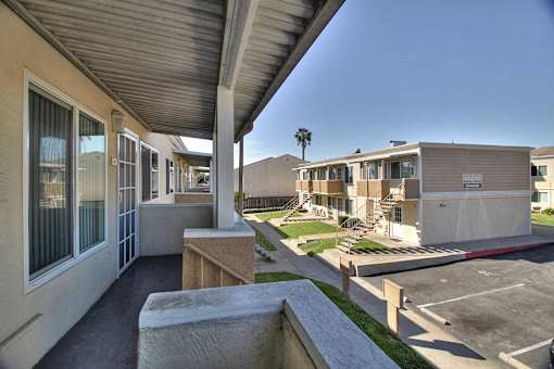 A view of a building's patio with a concrete wall and a parking lot in the background.
