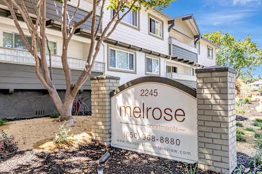 A sign for Melrose Apartments is in front of a building.