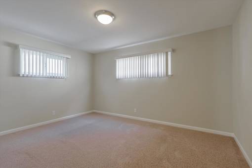 A room with carpeted floor and two windows.
