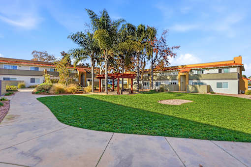 A building with a red roof is surrounded by a green lawn and palm trees.