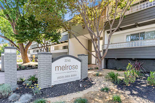 A sign for Melrose apartments is in front of a building.