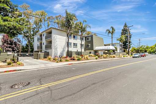 A street view of a residential area with apartment buildings and cars parked on the side of the road.