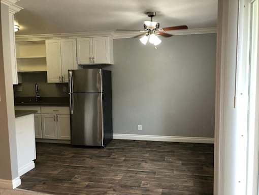 A kitchen with a refrigerator, cabinets, and a ceiling fan.