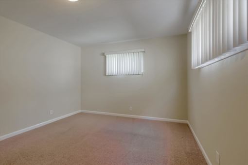 A room with a carpeted floor and a window with blinds.