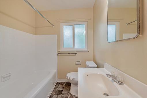 A white bathtub sits in a bathroom with a toilet and a window.
