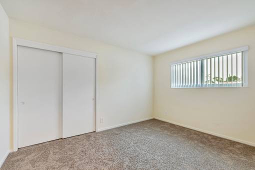 A room with a carpeted floor, a window with blinds, and a door.