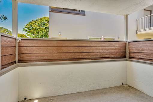 A balcony with a white wall and brown wooden slats.