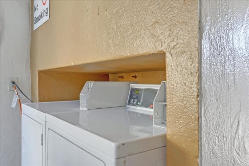 A washing machine in a small room with a no smoking sign on the wall.