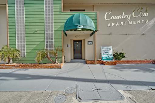 The front of the Country Club Apartments building with a green awning.