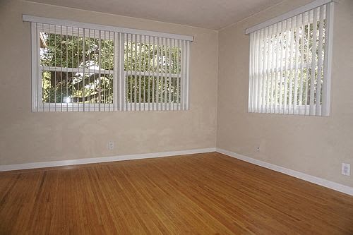 A room with wooden floors and white walls has two windows with blinds.
