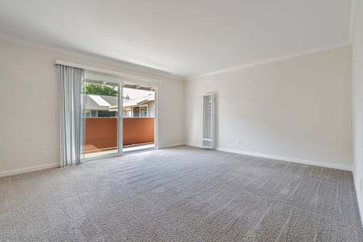 A room with a carpeted floor and a sliding glass door leading to a balcony.