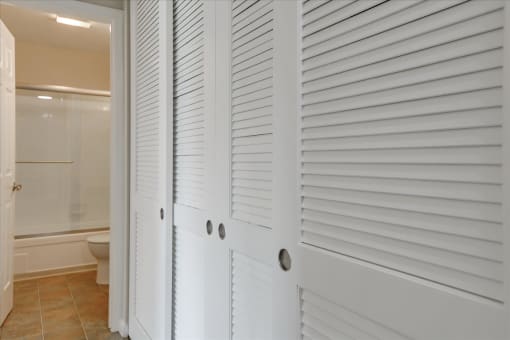 a white closet with white shuttered doors in a bathroom