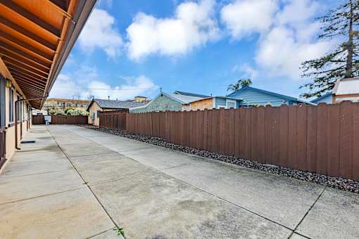 A long concrete driveway leads to a house with a brown fence on the side.