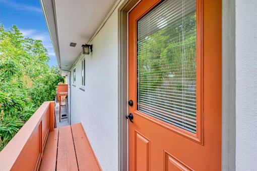A balcony with a wooden bench and an orange door.