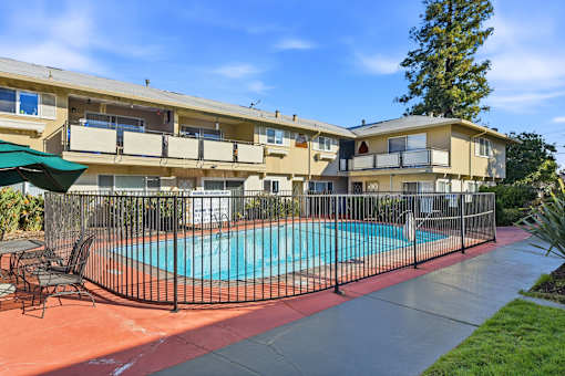 A pool surrounded by a black fence and chairs.
