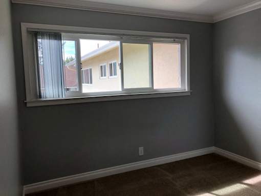 A room with a window and a carpeted floor.