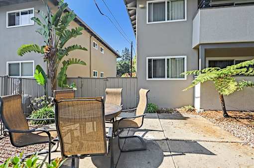 A patio with a table and chairs is surrounded by a fence and a tree.