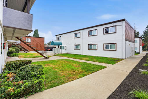 A white building with a brown roof is surrounded by a green lawn and a sidewalk.