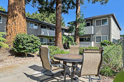 A patio with a table and chairs is surrounded by trees and houses.
