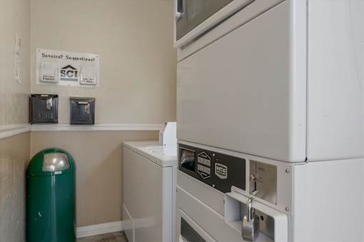 A white dishwasher is in a kitchen with a green trash can.