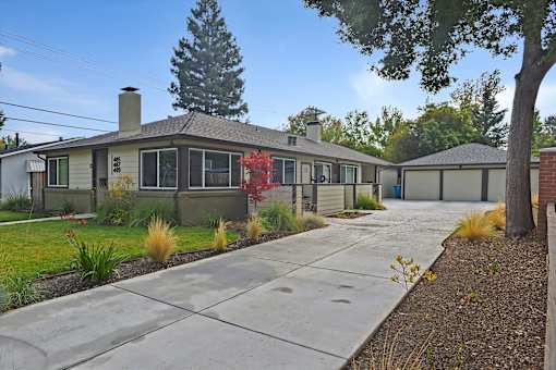 A house with a grey roof and a grey wall with a red plant in front.